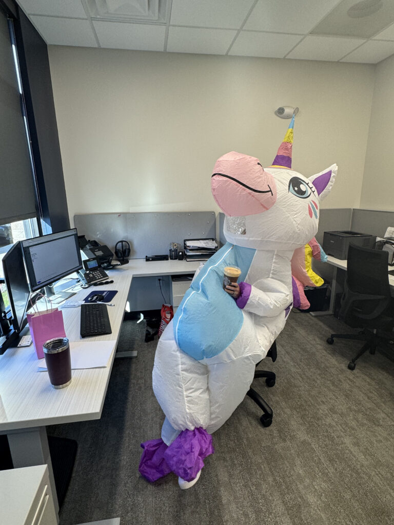 Dentist in Altoona IA wearing a unicorn costume with coffee, relaxing while sitting in a desk chair with legs crossed