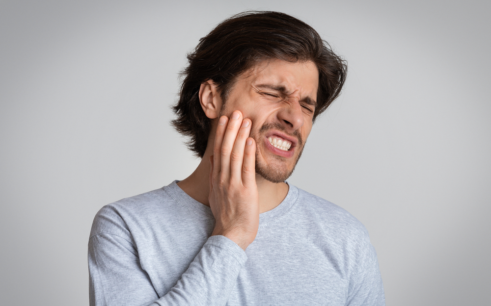 A man holding his cheek in pain, probably in need of Emergency Dentistry
